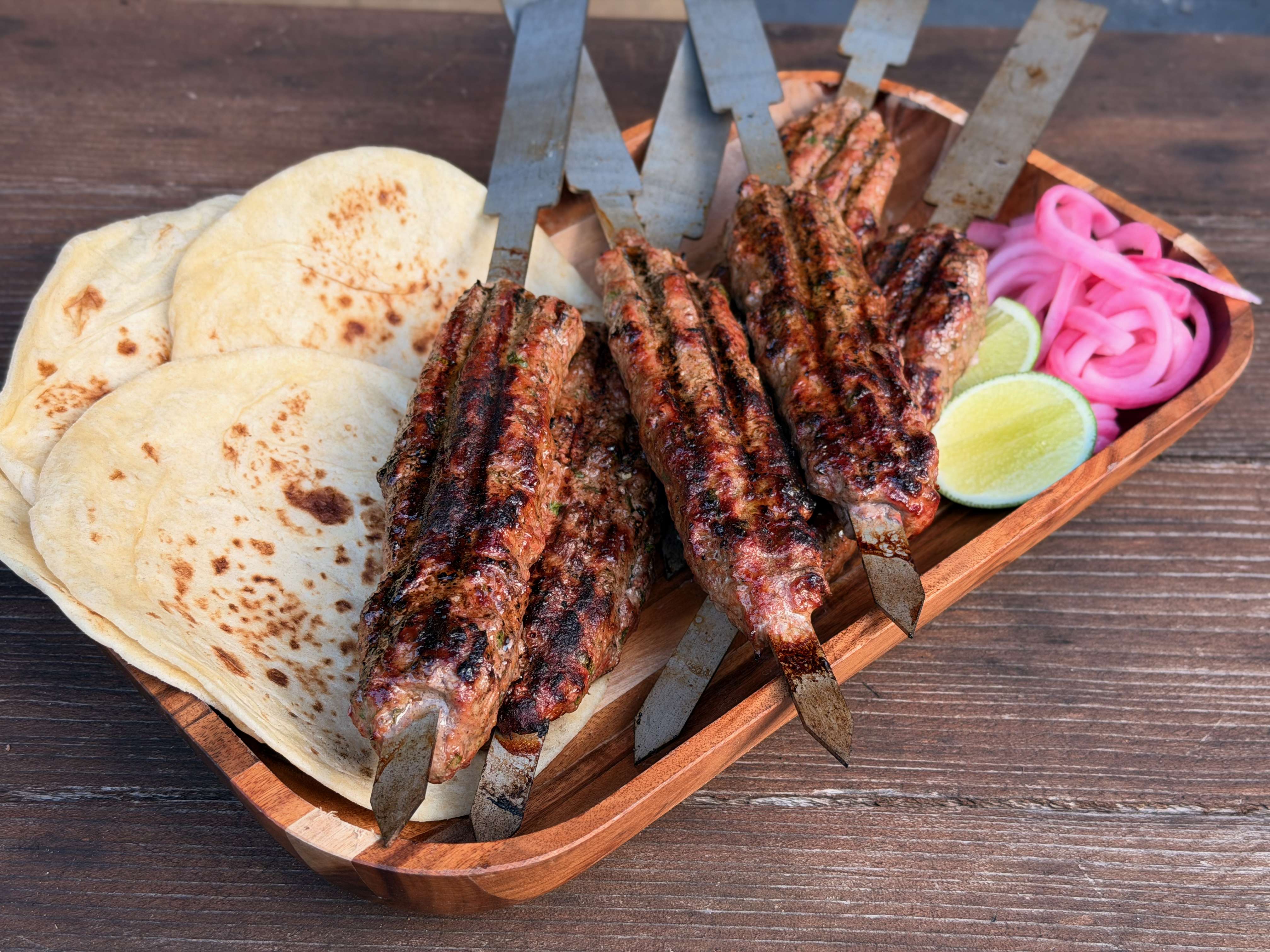 A platter of lamb kebabs on skewers with tortillas and assorted toppings.
